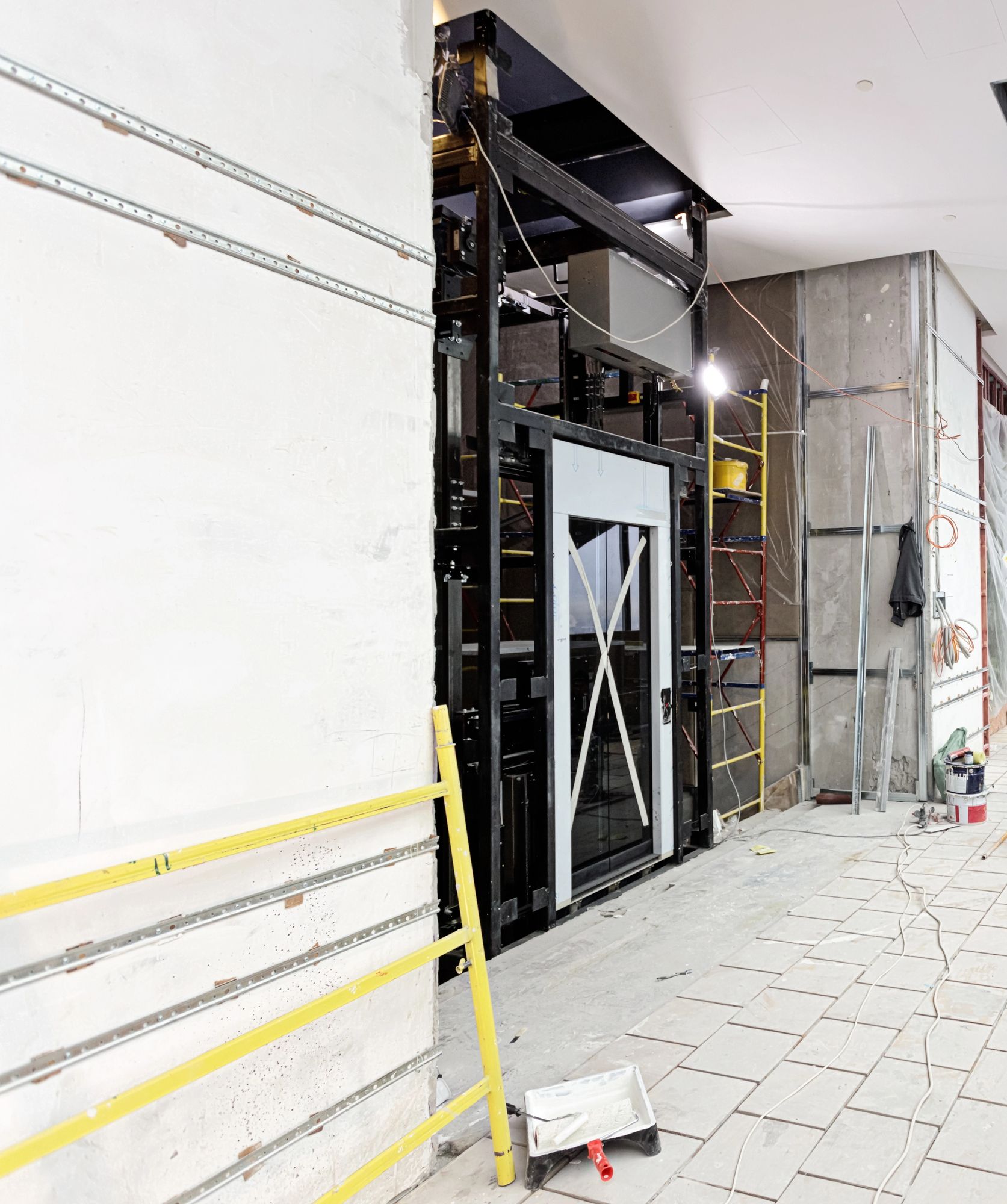 Cantiere edile interno con parete non rifinita, struttura metallica, scala e pavimento piastrellato.