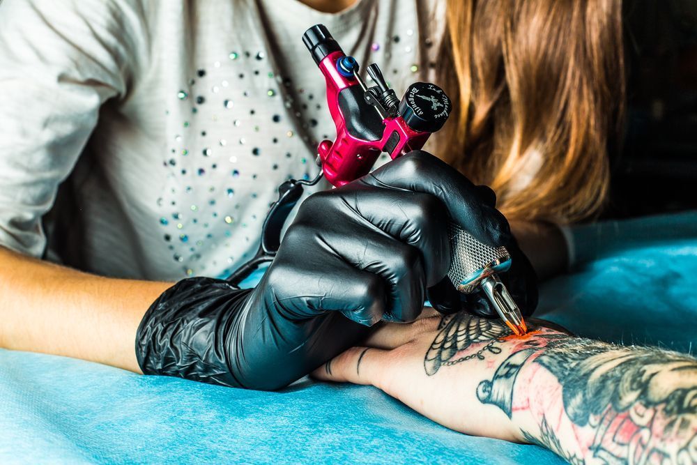 Tattoo Artist With Black Gloves Using Tattoo Machine On A Person's Wrist, Adding To Existing Tattoos  — Tattoo Inc Studio in Surfers Paradise, QLD