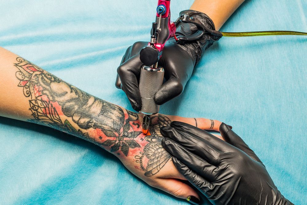 A Tattoo Artist Is Working On A Person's Forearm And Hand; Both Are Covered In Tattoos — Tattoo Inc Studio in Surfers Paradise, QLD