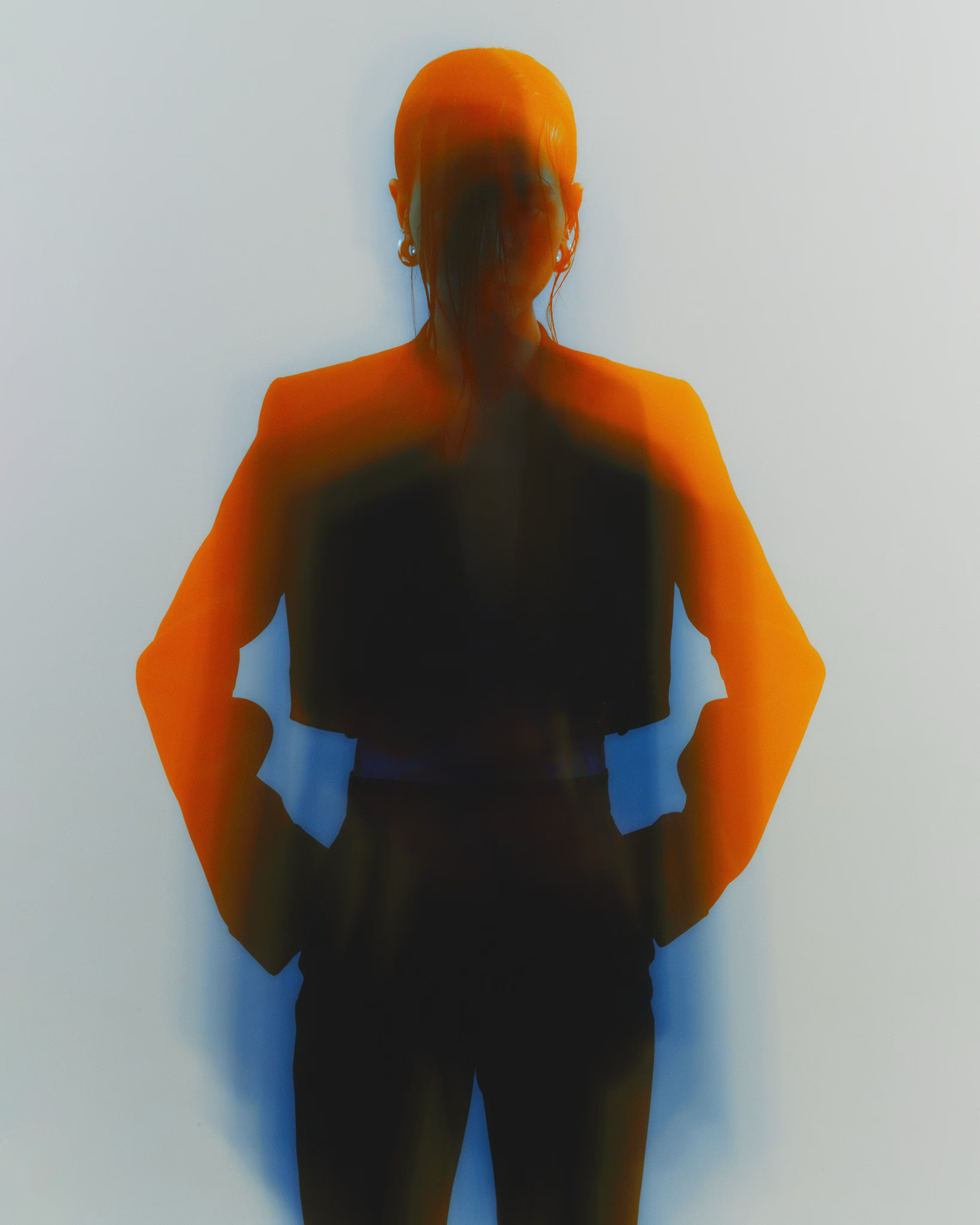 Silhouette of a person with hands on hips, wearing a blazer against a blurred orange and blue background. — Tattoo Inc Studio In Broadbeach, QLD
