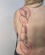 Back tattoo reading “In Christ Alone” in flowing script on a woman’s upper back.