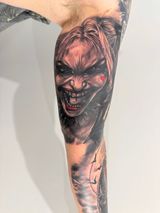 Close-up of a forearm tattoo showing a menacing red-haired monster face in dark black and red ink