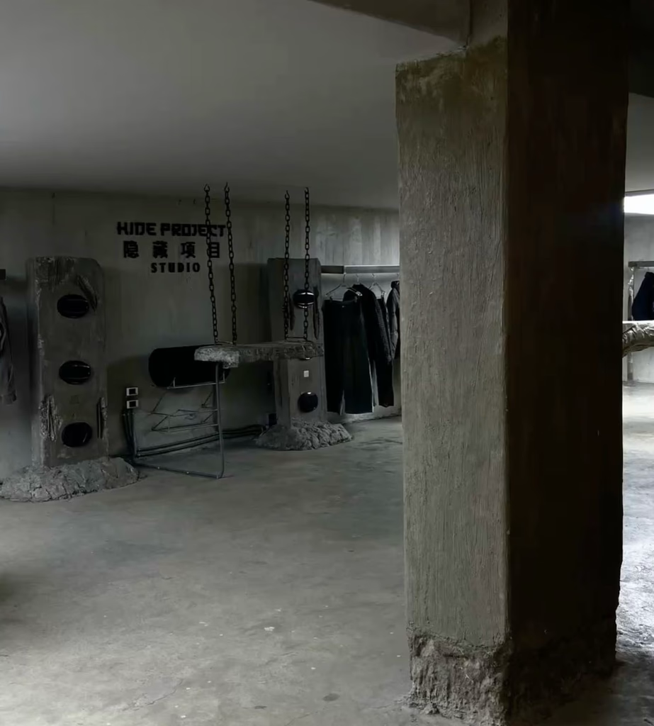 Concrete-walled studio space with raw aesthetic. Features concrete pillars, clothing racks, and speakers.