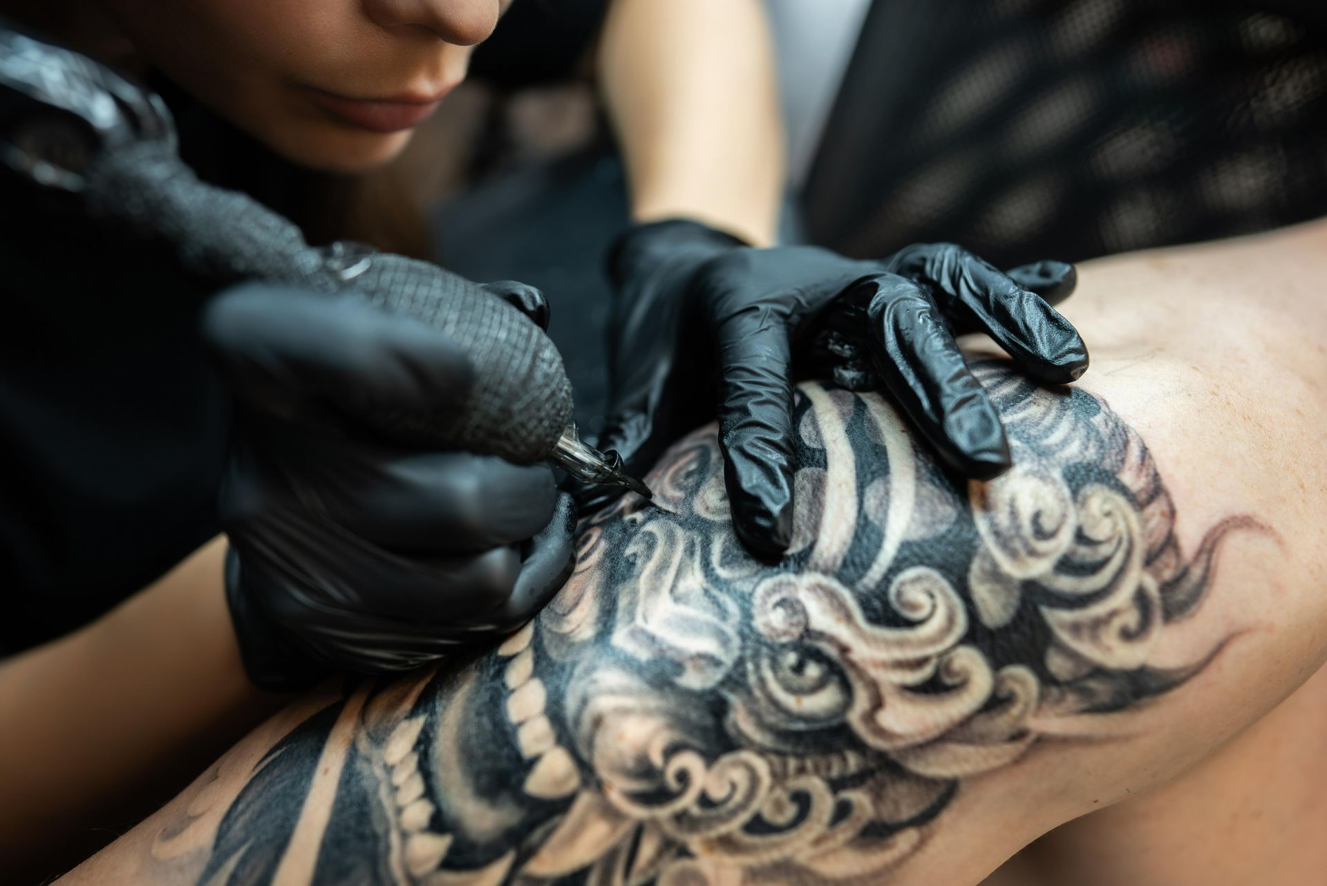 Tattoo Artist With Black Gloves Using A Tattoo Machine, Inking A Detailed Design On A Knee  — Tattoo Inc Studio in Surfers Paradise, QLD