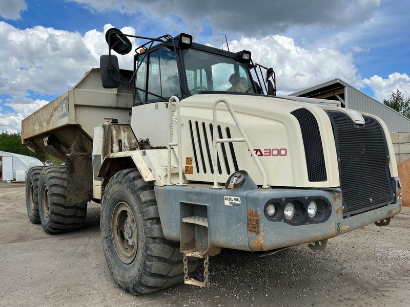 Off-white Terex TA300 articulated dump truck on gravel, outdoors under a cloudy sky.