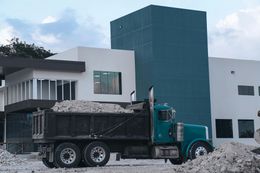 Dump truck filled with rubble in front of a modern building under construction.