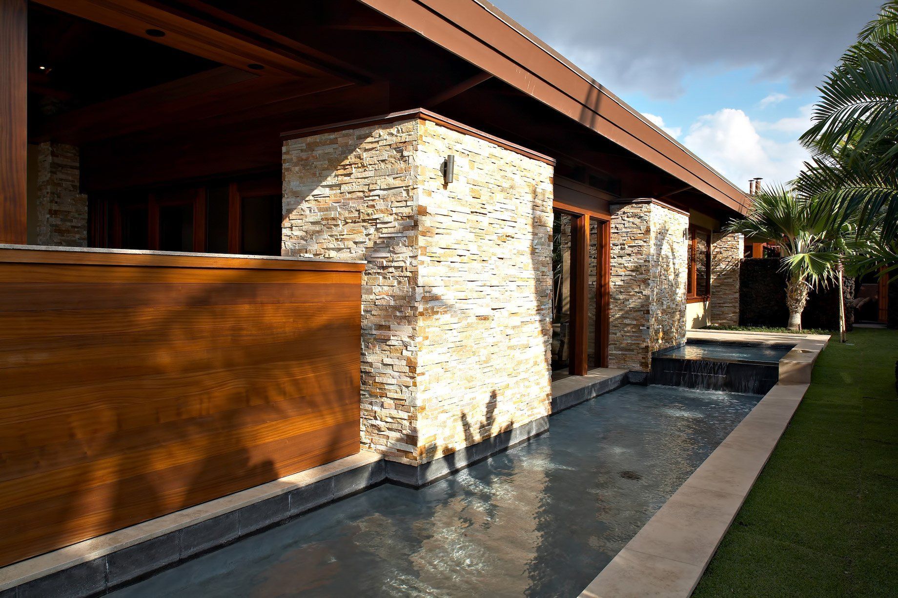 Modern house with stone pillars, dark wood trim, and a reflecting pool.