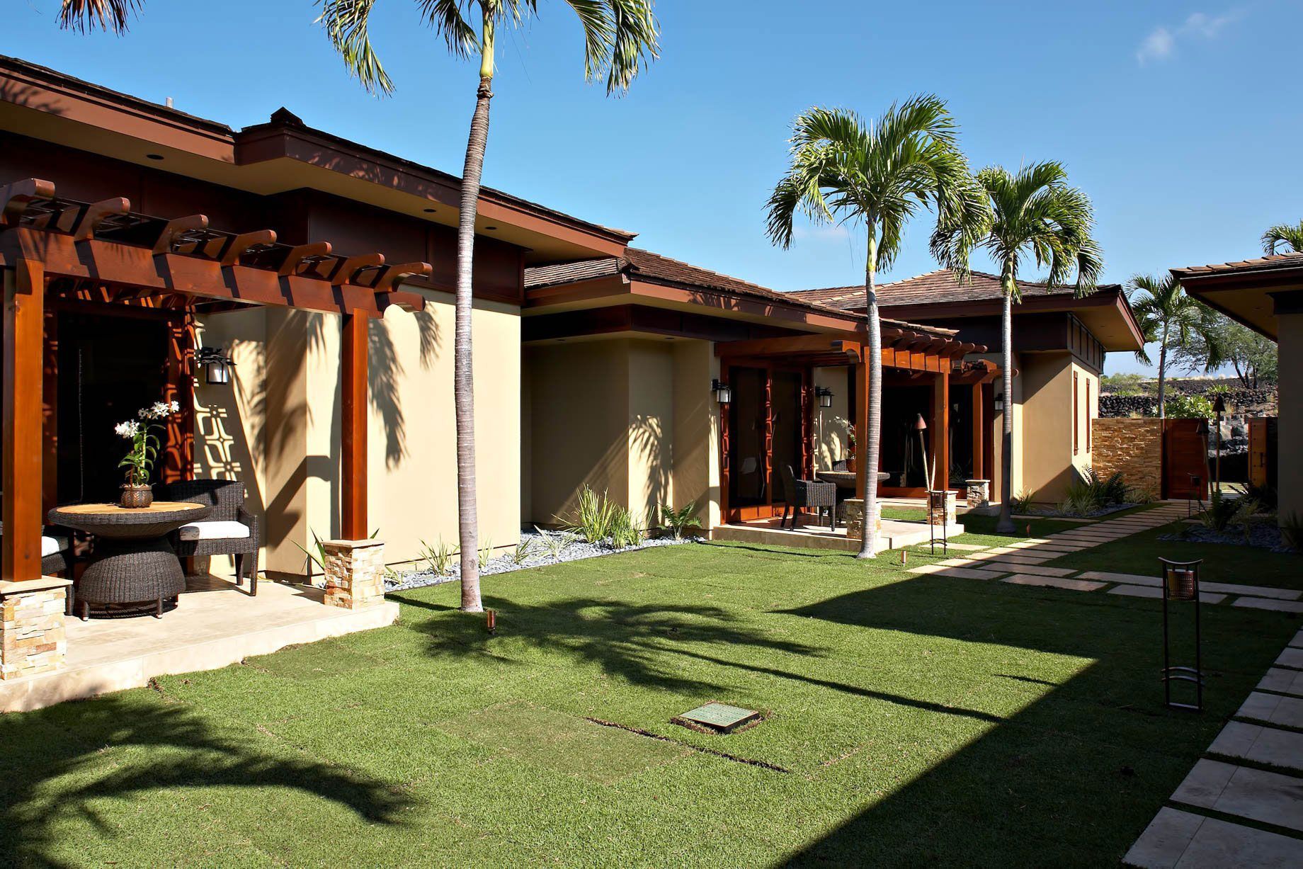 Luxurious tropical homes with lush green lawn and palm trees under a bright blue sky.