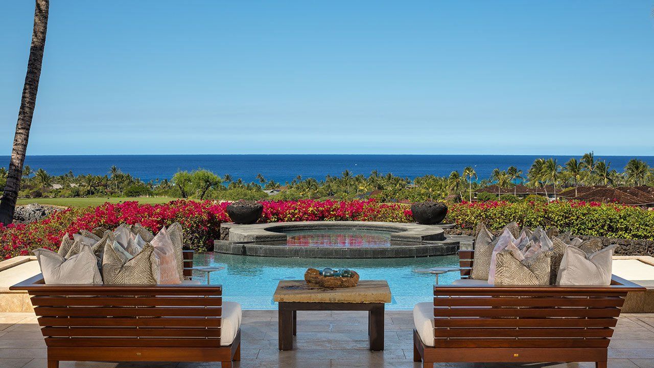 Poolside view of ocean; wooden lounge chairs, red flowers, blue sky, and water.
