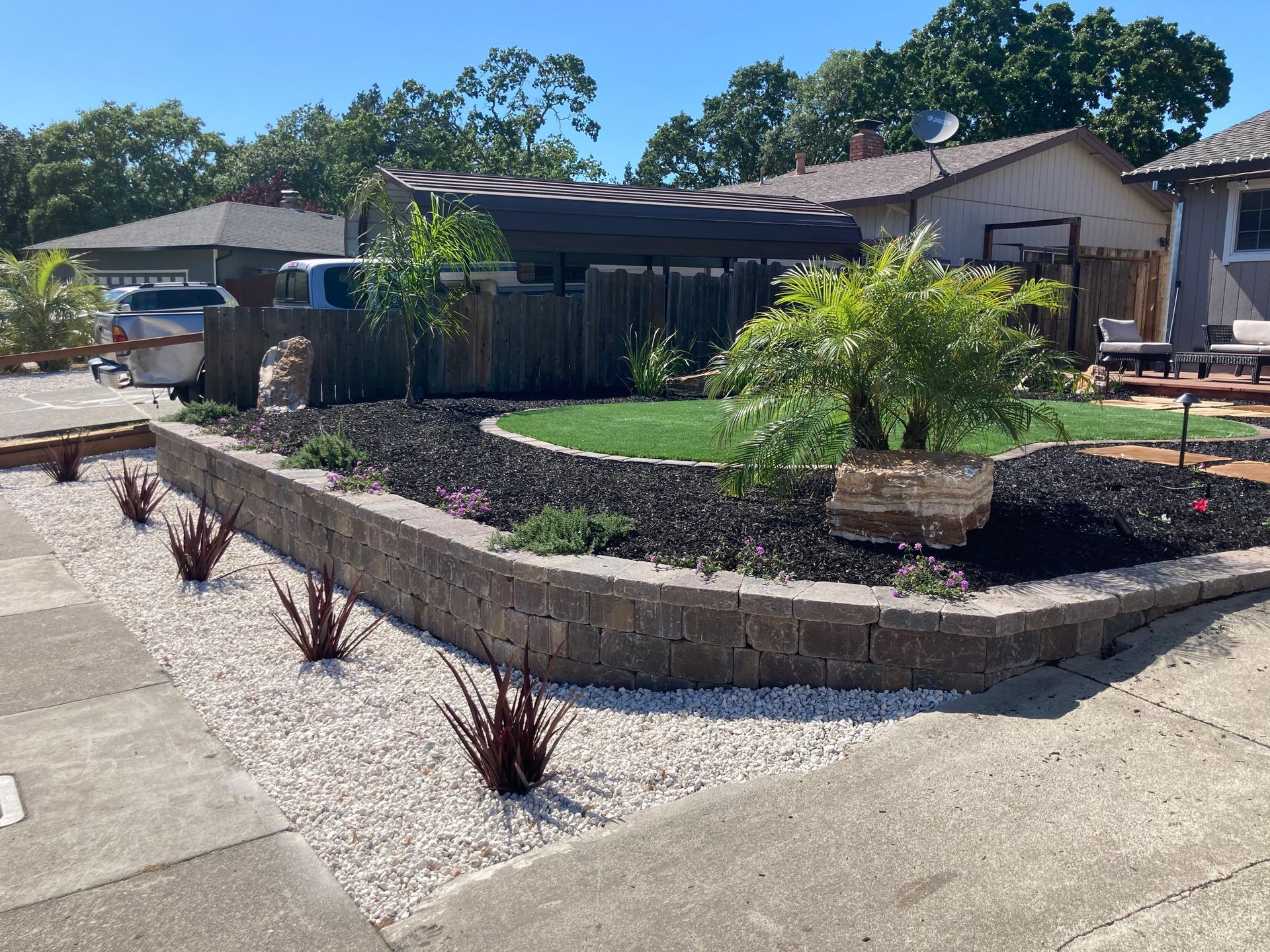 A front yard with a stone retaining wall, landscaping, and a lawn on a sunny day.