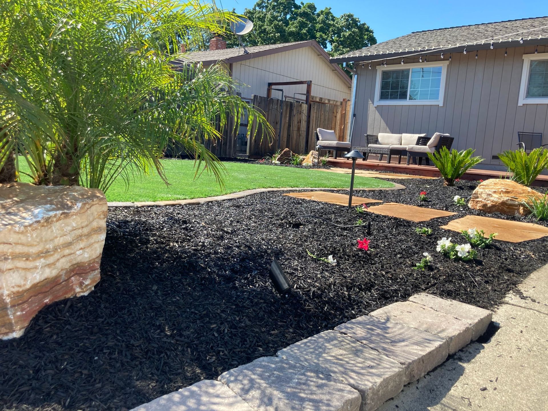 Front yard with black mulch, stone steps, and manicured lawn. Brown house in background.
