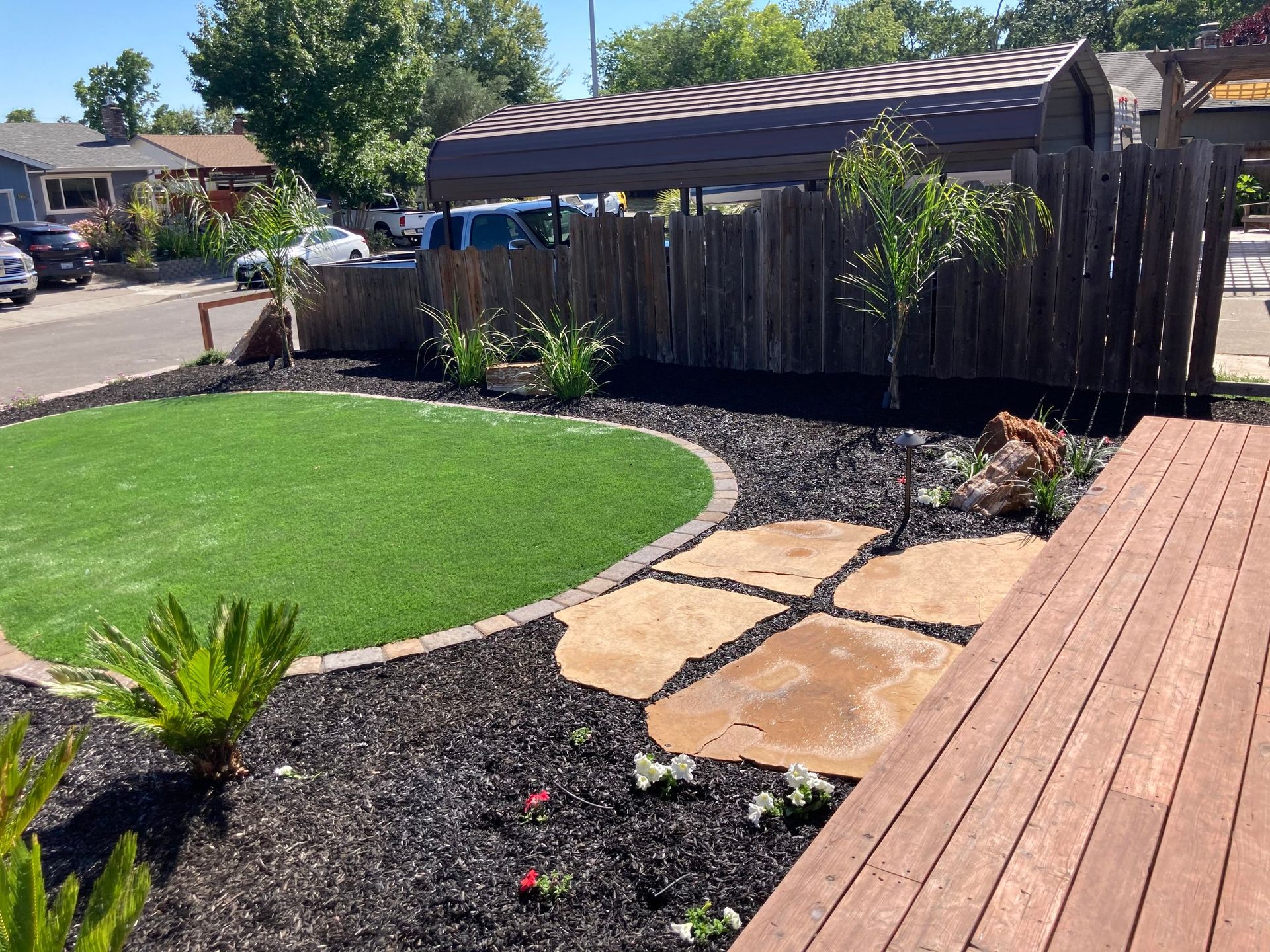 A front yard with artificial turf, a stone path, dark mulch, plants, and a wooden fence.