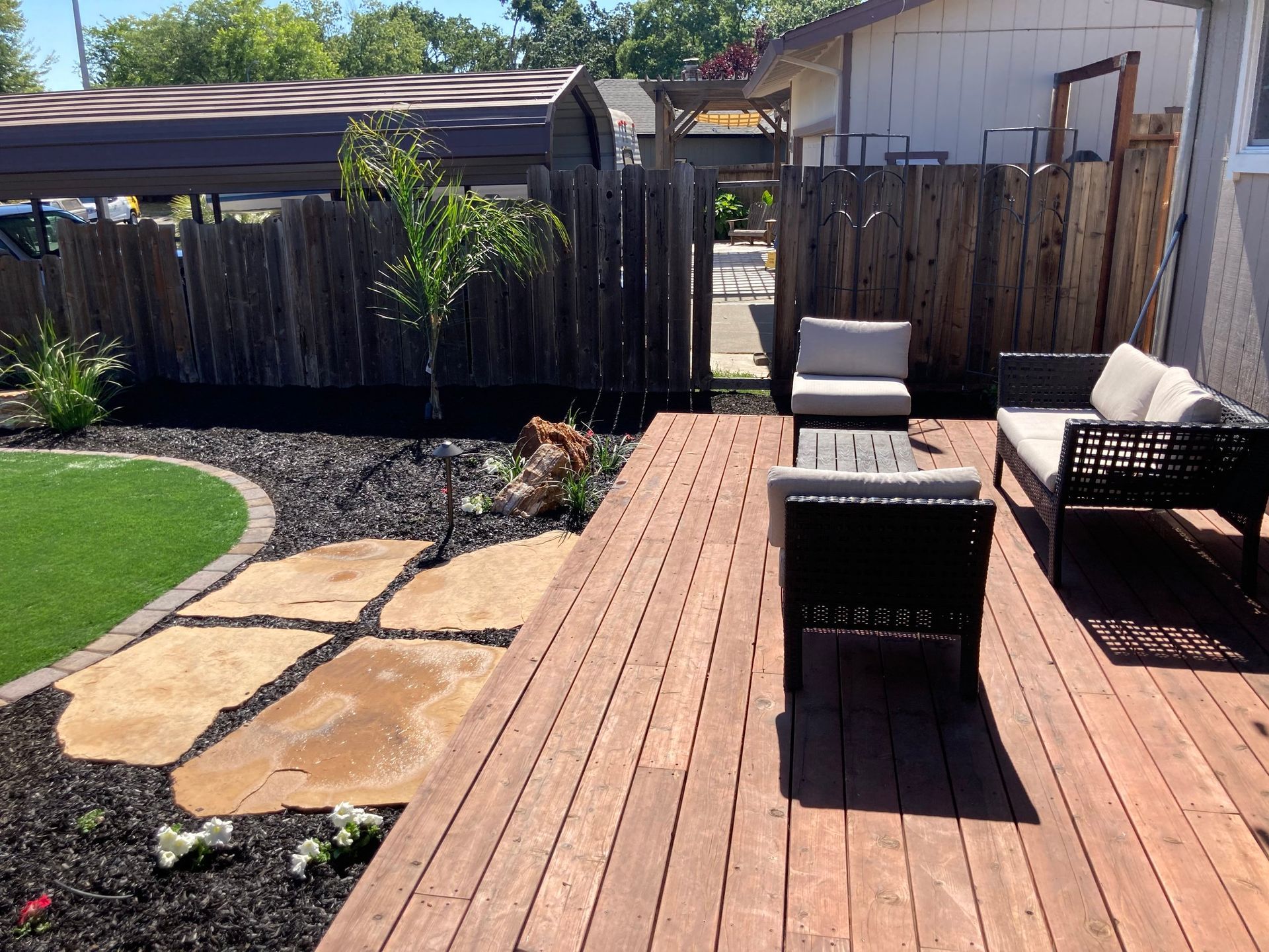 Wooden deck with patio furniture, stone path, and fenced backyard with artificial grass.