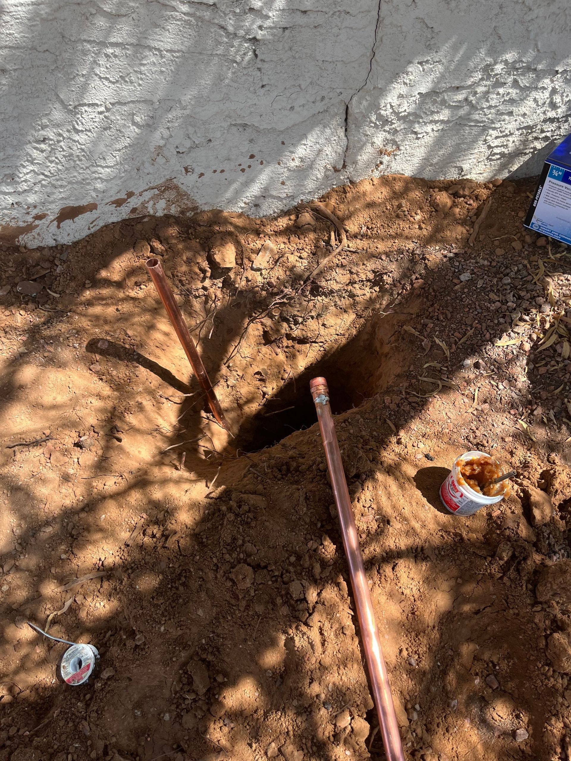 Copper pipes protruding from soil near a white wall, possibly for plumbing.