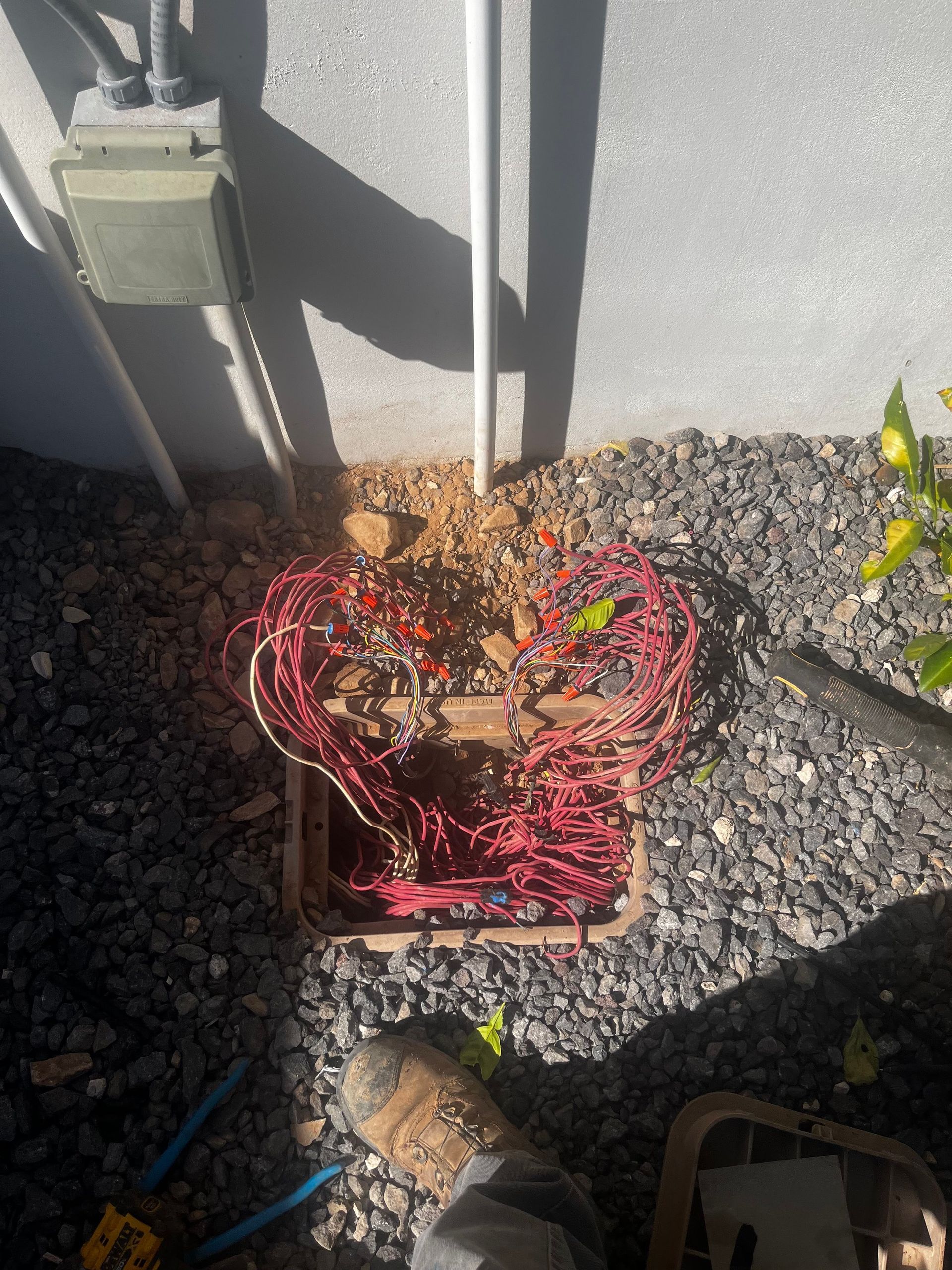 Open utility box with tangled red wires, near a building's exterior. Person's foot visible.