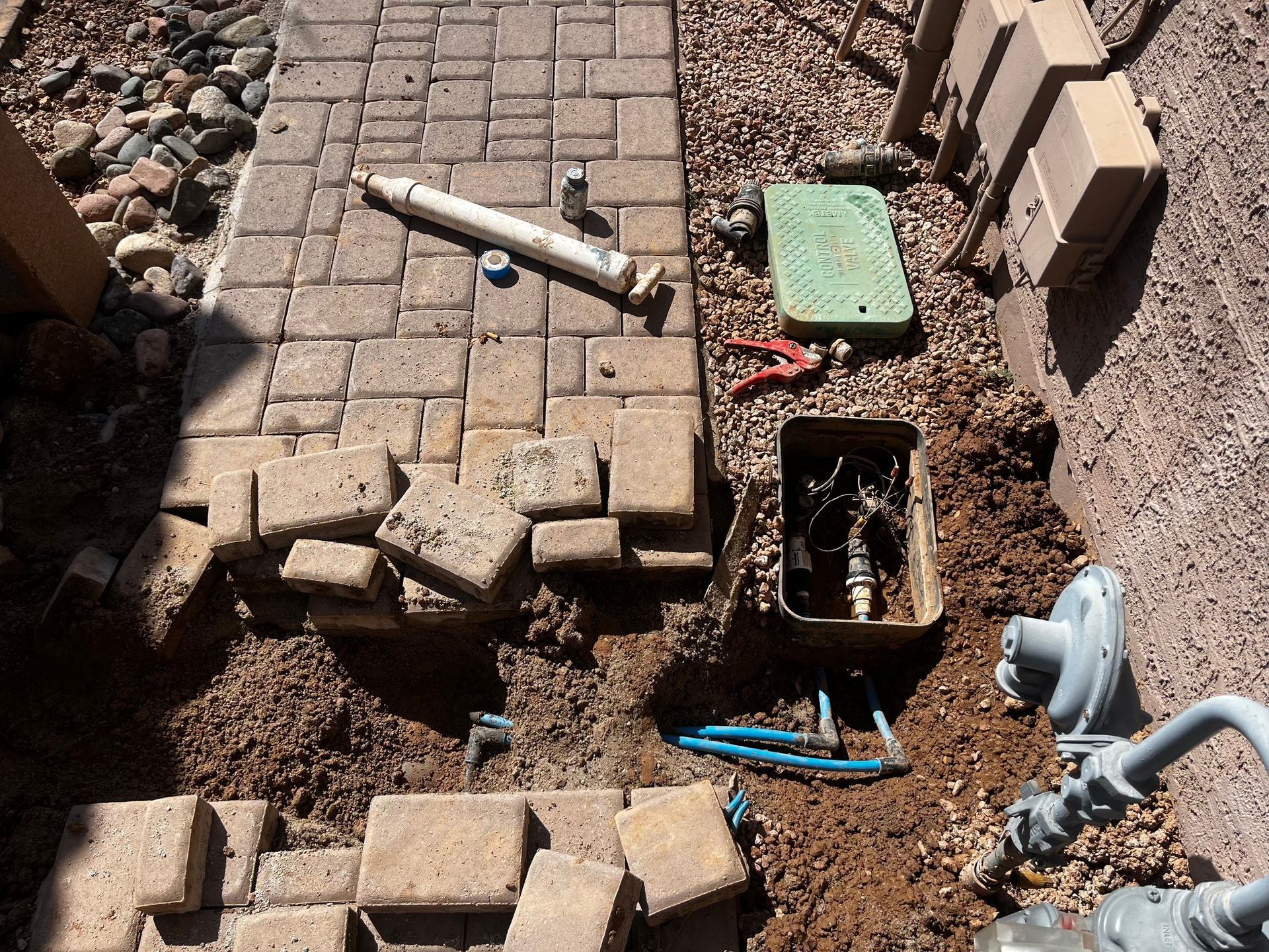 Construction site: bricks removed to access underground water pipes and gas meter near a building.