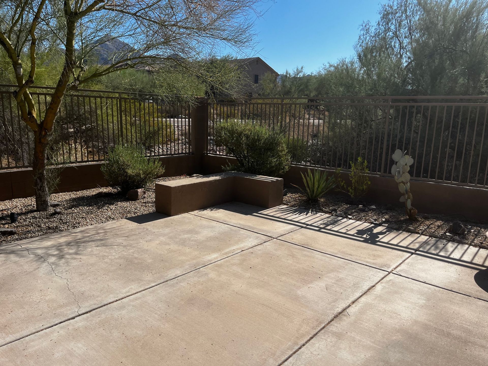 Concrete patio with low walls, fence, and desert landscaping under a bright blue sky.
