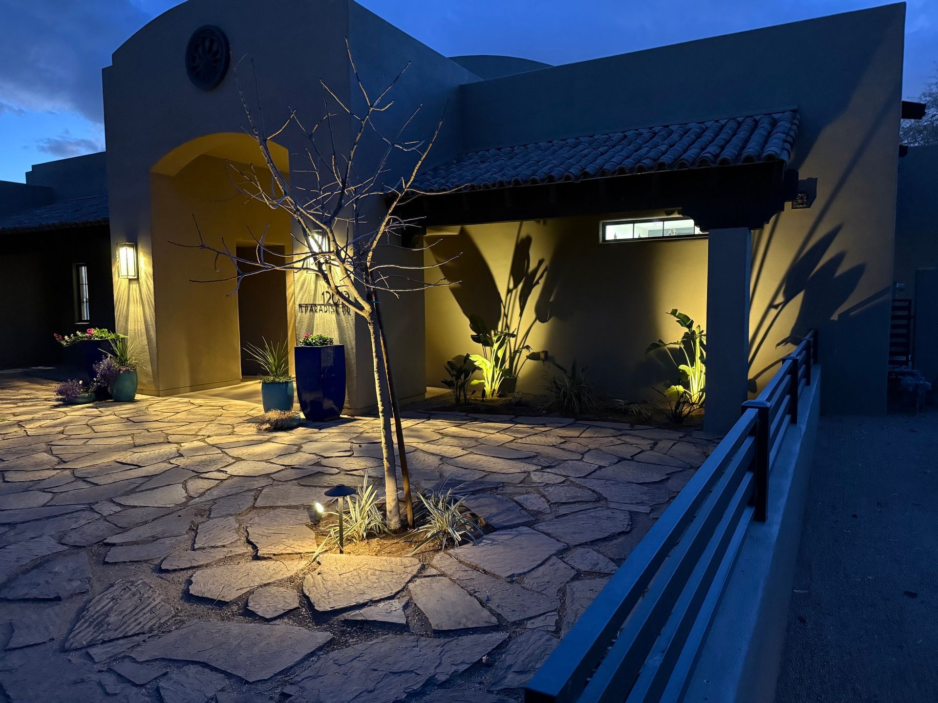 Exterior view of a house at dusk, with outdoor lighting illuminating the stone patio and facade.