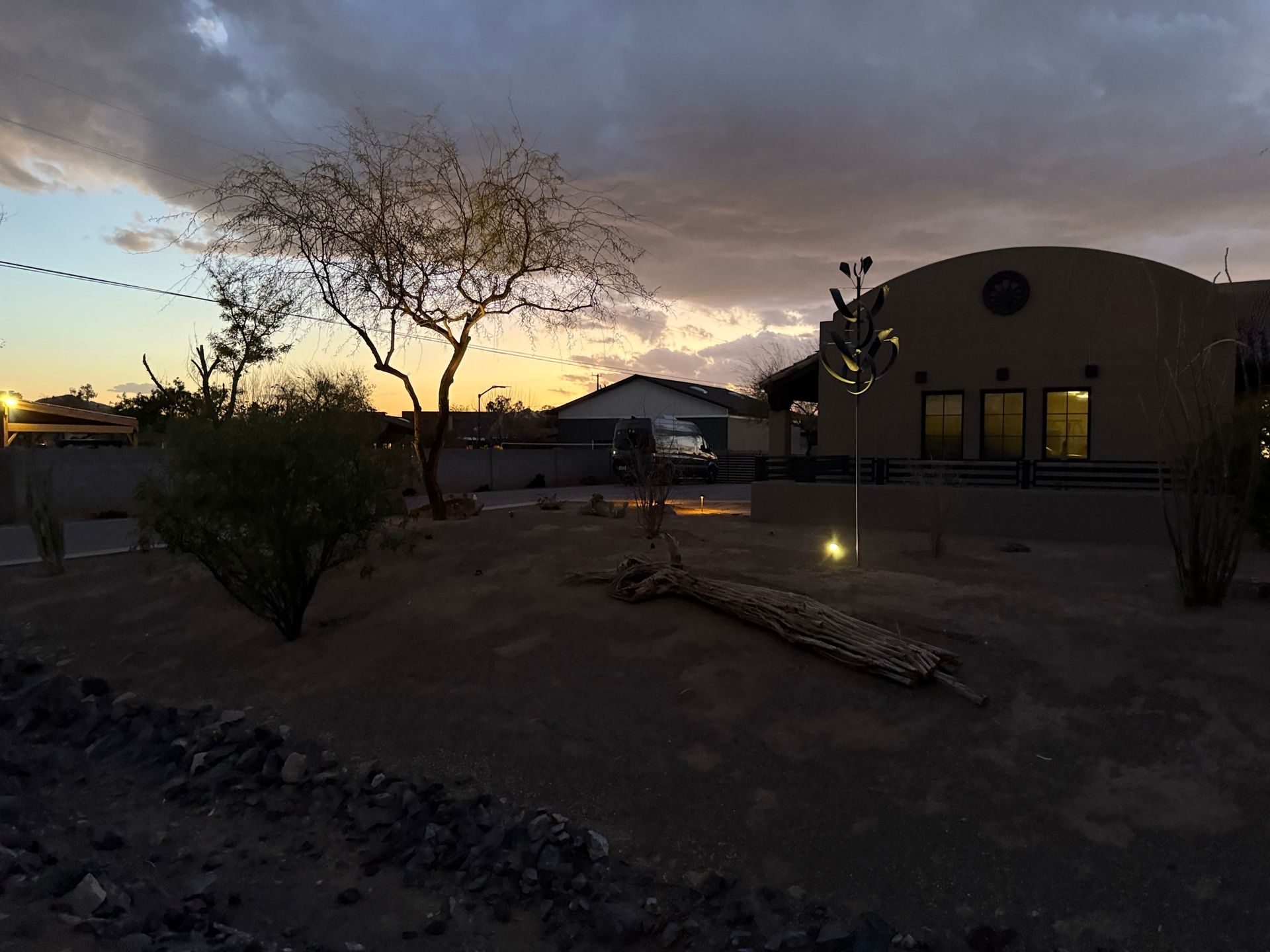 Desert landscape at dusk with a building, trees, and a cloudy sky.