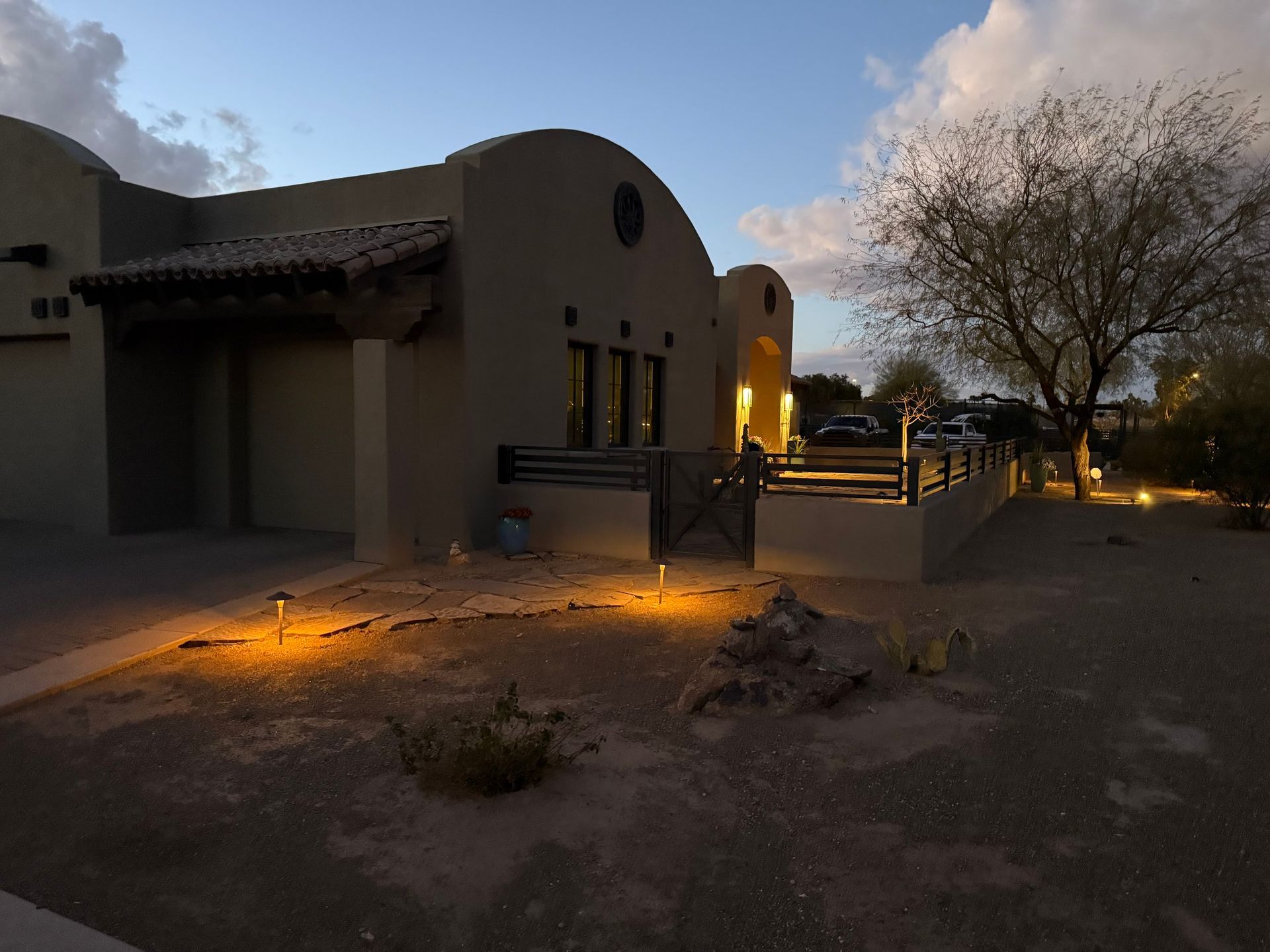 Adobe-style house with warm landscape lighting at dusk.