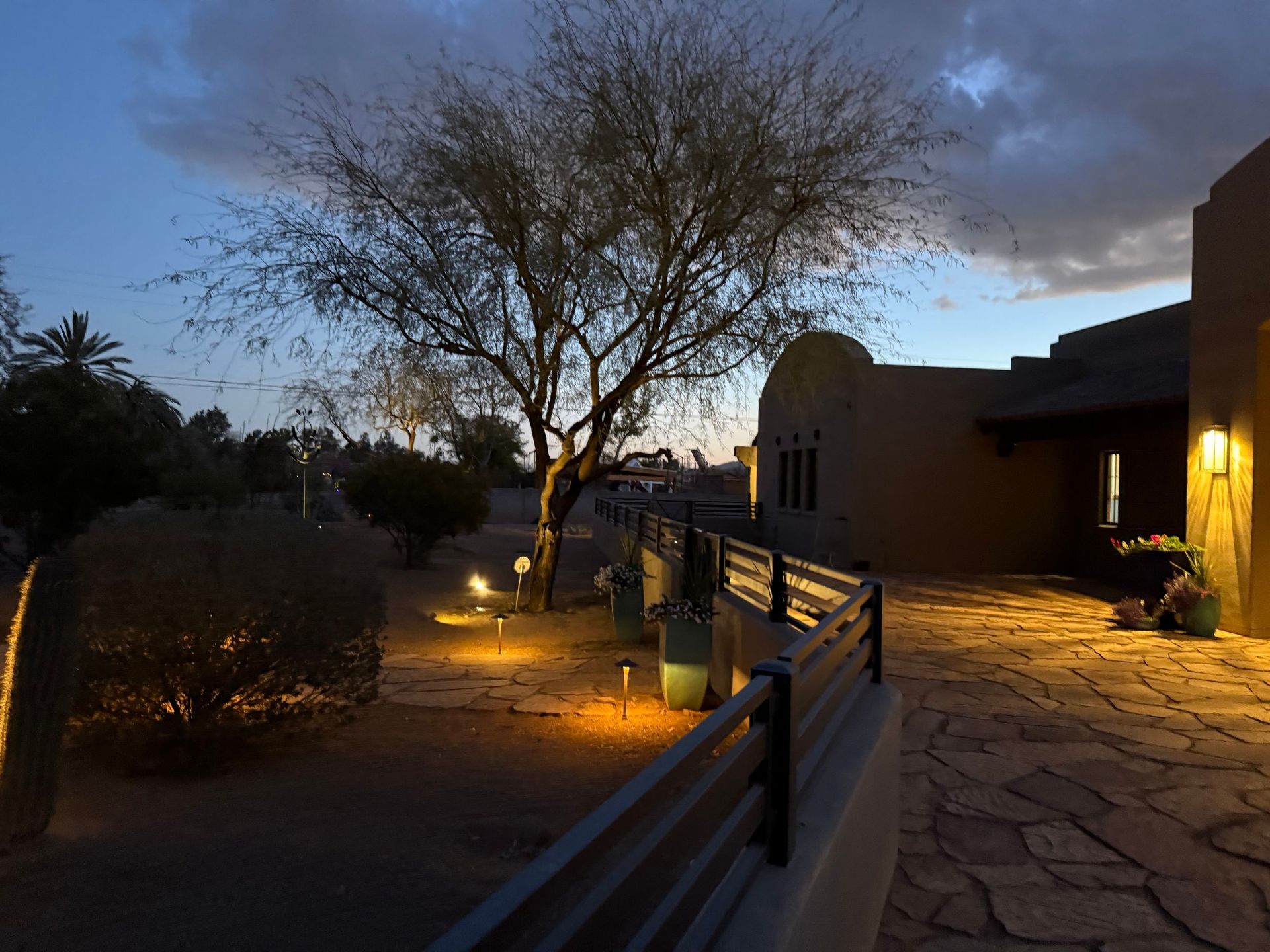 Night scene: illuminated desert landscape with a tree, pathway, and adobe-style building.