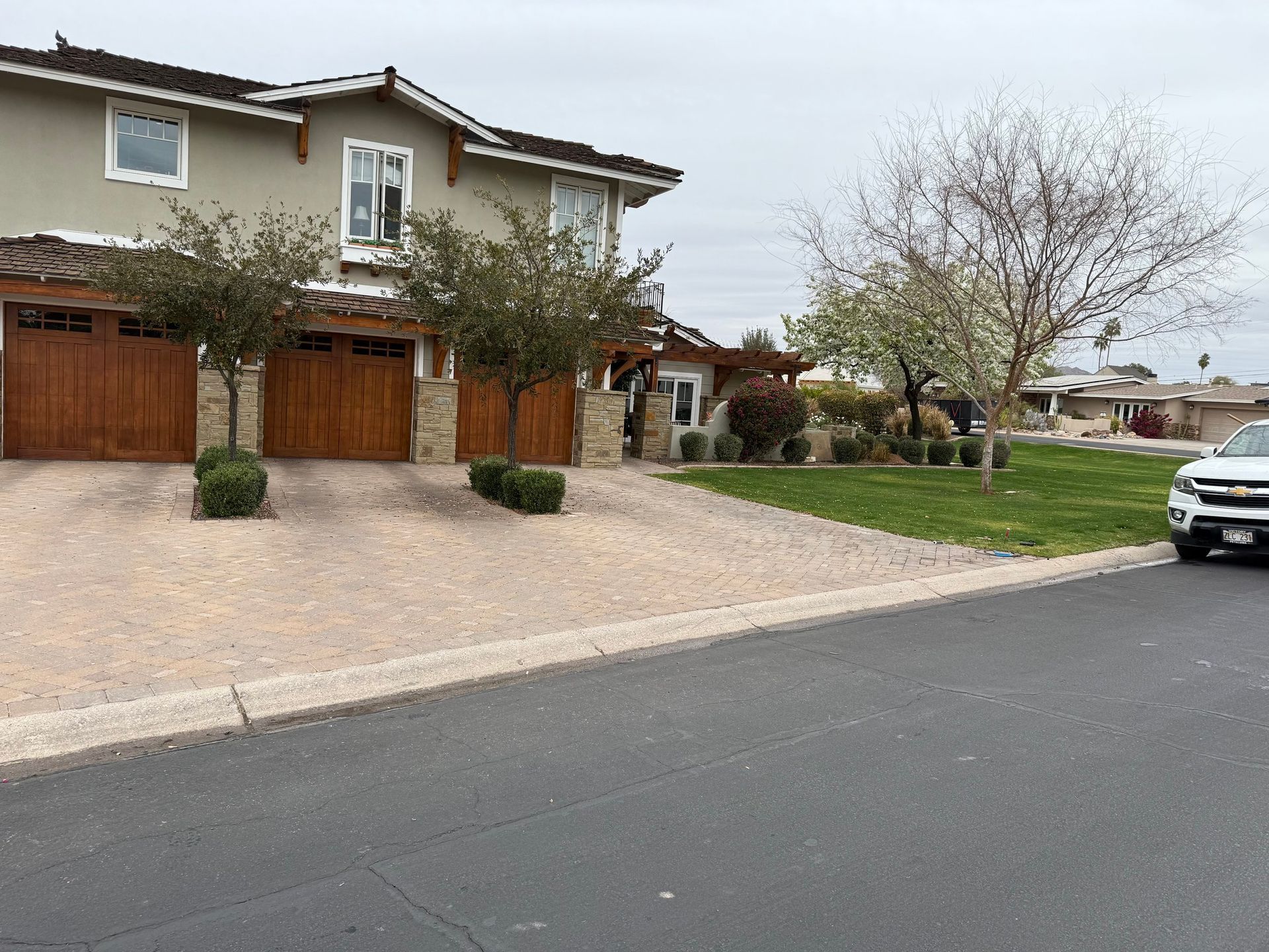 Two-story beige house with brown garage doors, a gravel driveway, and a small tree in front.