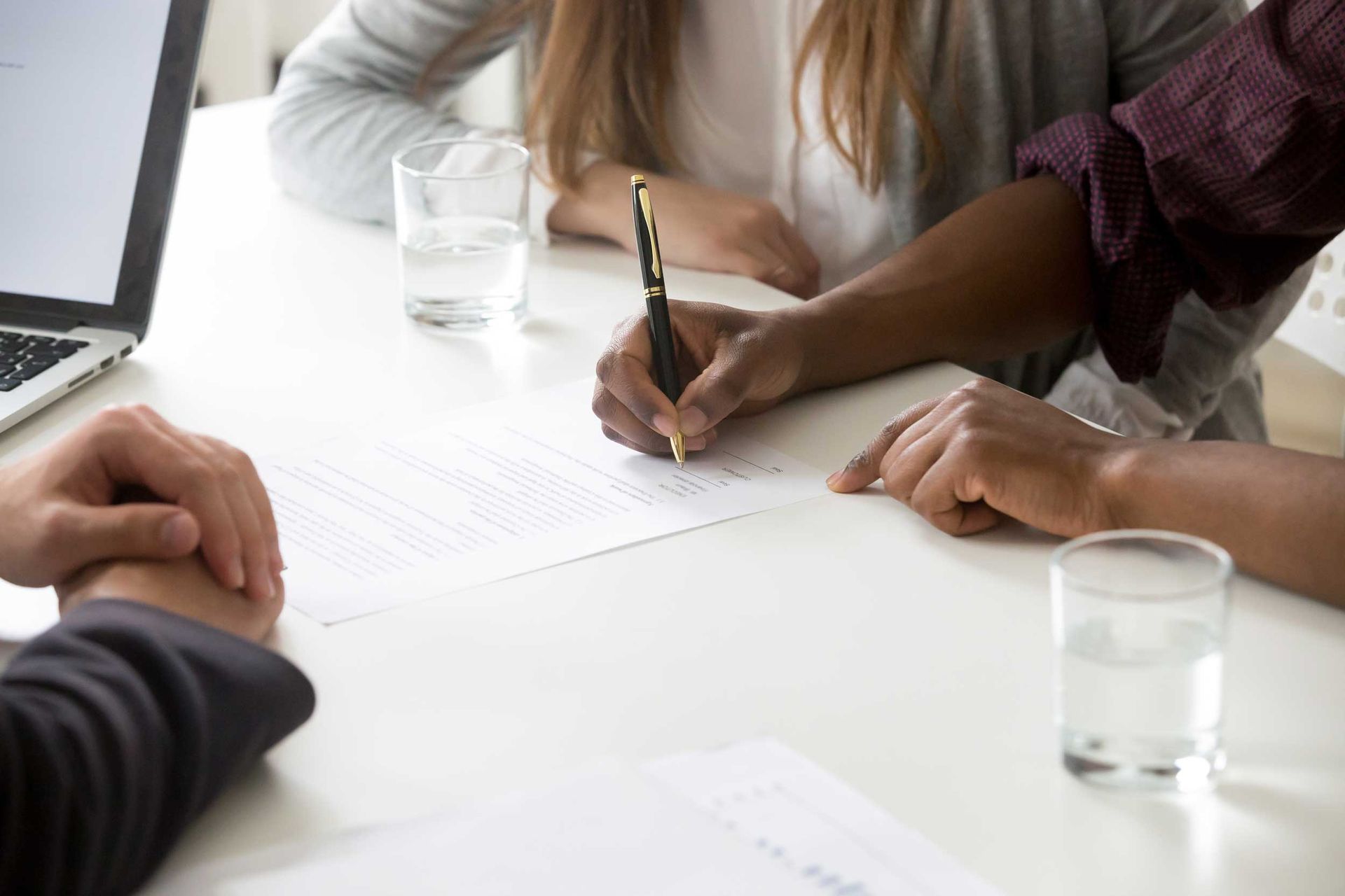 A partial view of a man next to his partner signing a document at a lawyer’s desk.