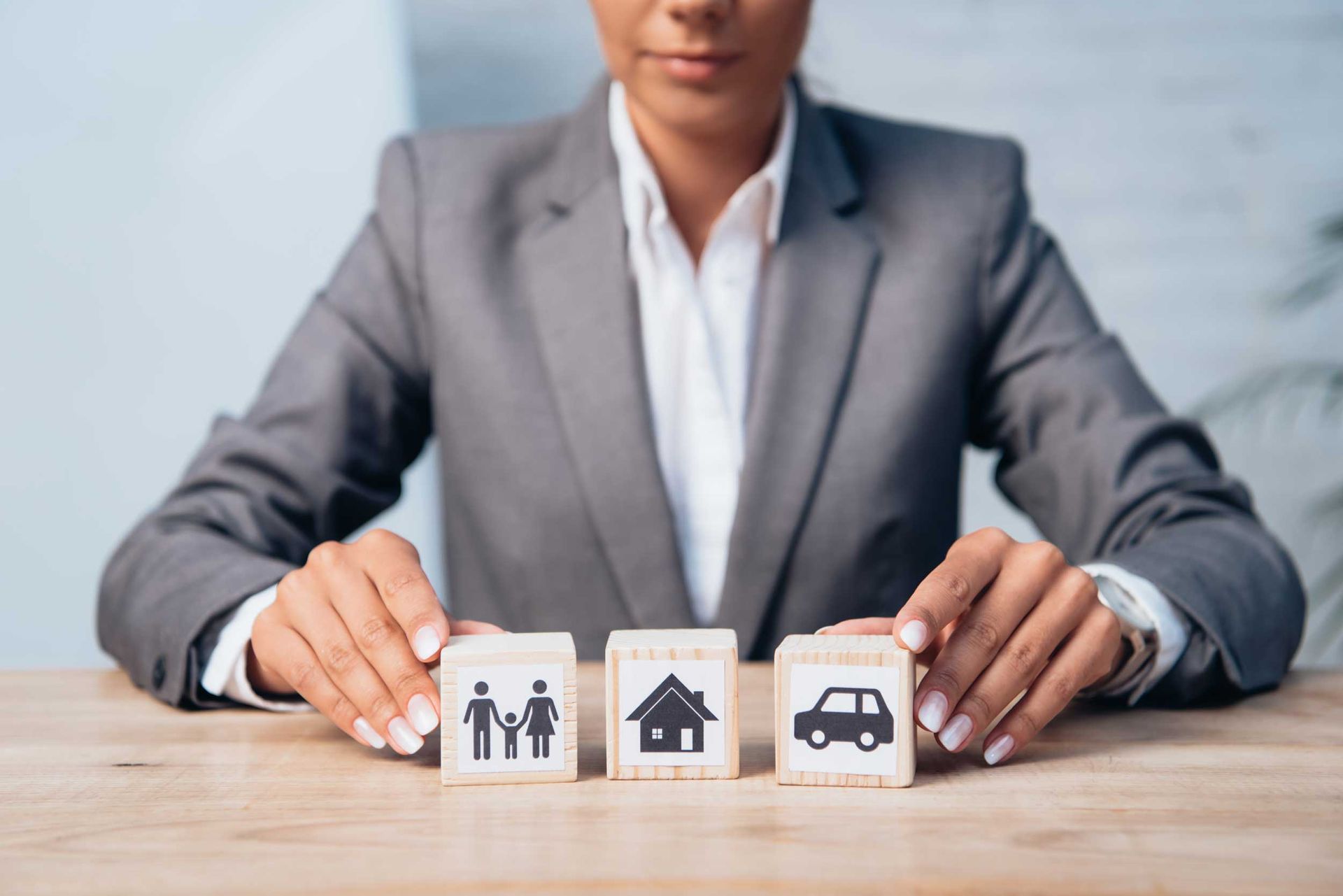A cropped view of a lawyer touching wooden cubes with family, car, and house images on them.