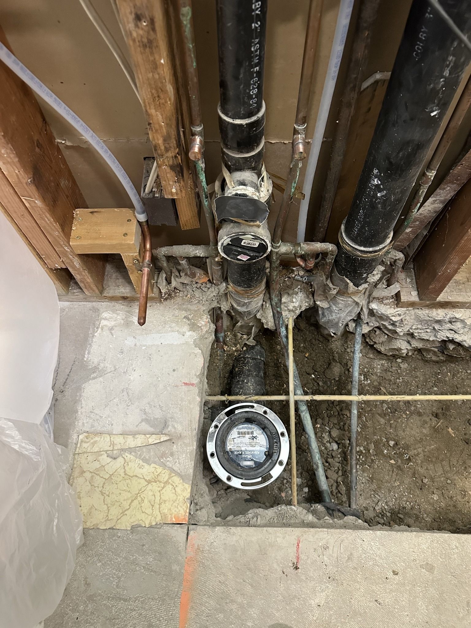 Plumbing pipes and a floor drain are exposed under a structure, with concrete and wood visible.