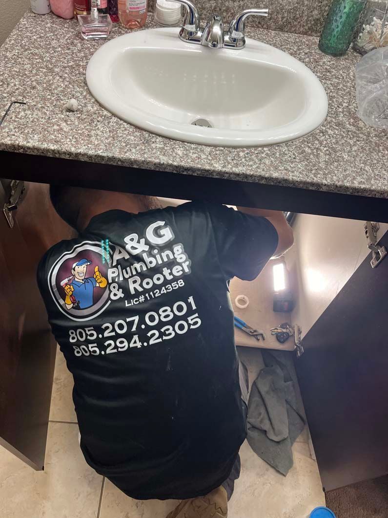 Plumber fixing a leaky white pipe under a sink with a red wrench; water is spraying.