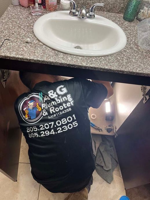 Plumber tightening pipe on water heater in a tiled bathroom, using a wrench.