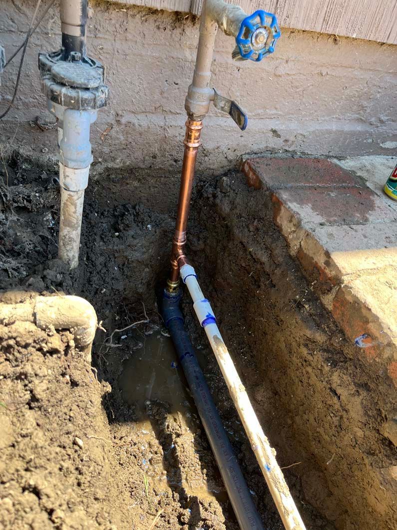 Plumbing pipes and a floor drain are exposed under a structure, with concrete and wood visible.