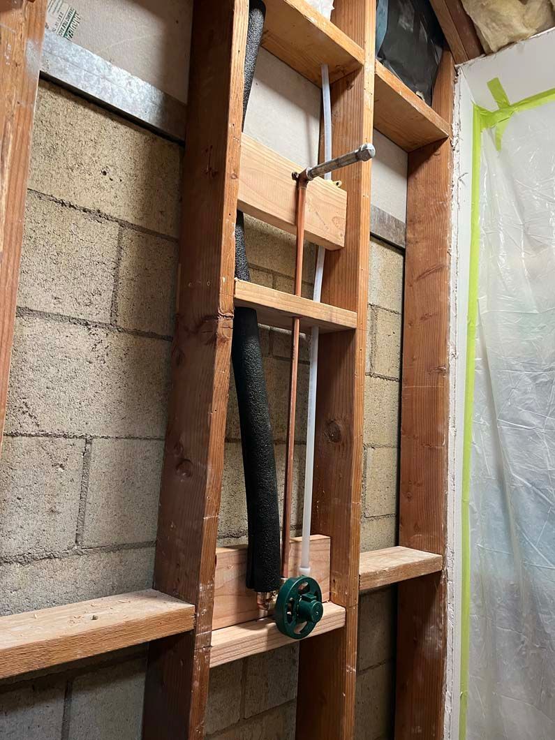 Copper water pipe exposed in a hole, leading to a spigot attached to a wall; soil surrounds.