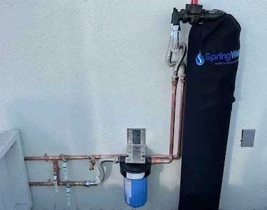 Water filtration system with copper pipes and a blue filter on a wall.