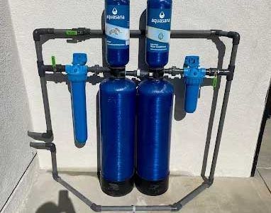 Blue water filtration system with multiple filters and pipes against a light wall.