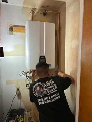 Plumber installing a water heater; copper pipes visible. A&G Plumbing shirt.