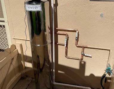 Stainless steel water filter system installed outside. Copper pipes and white PVC.