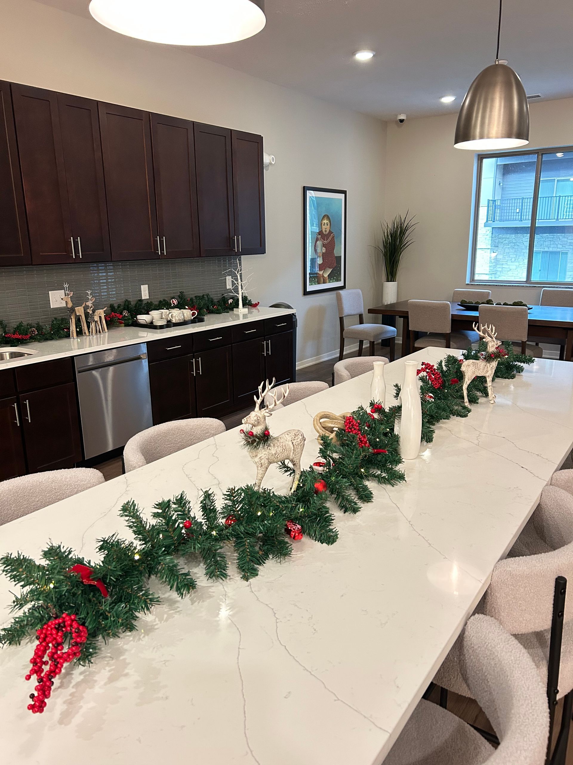 Decorated conference room with long tables, garland centerpiece, cabinets, windows, and pendant lights.