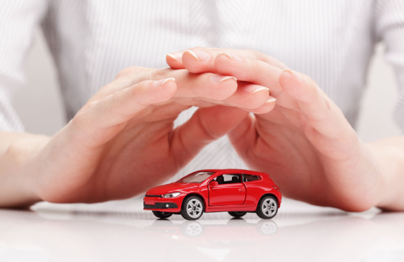 Hands cupped over a small red toy car on a white surface, symbolizing protection.