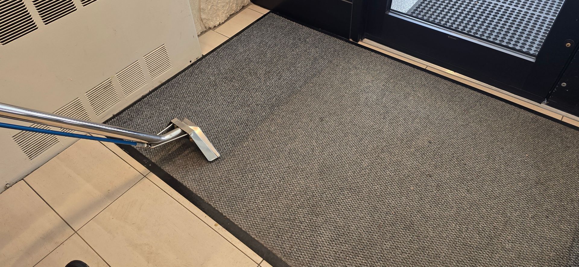 A vacuum cleaner cleaning a gray carpet in a room with light brown walls.