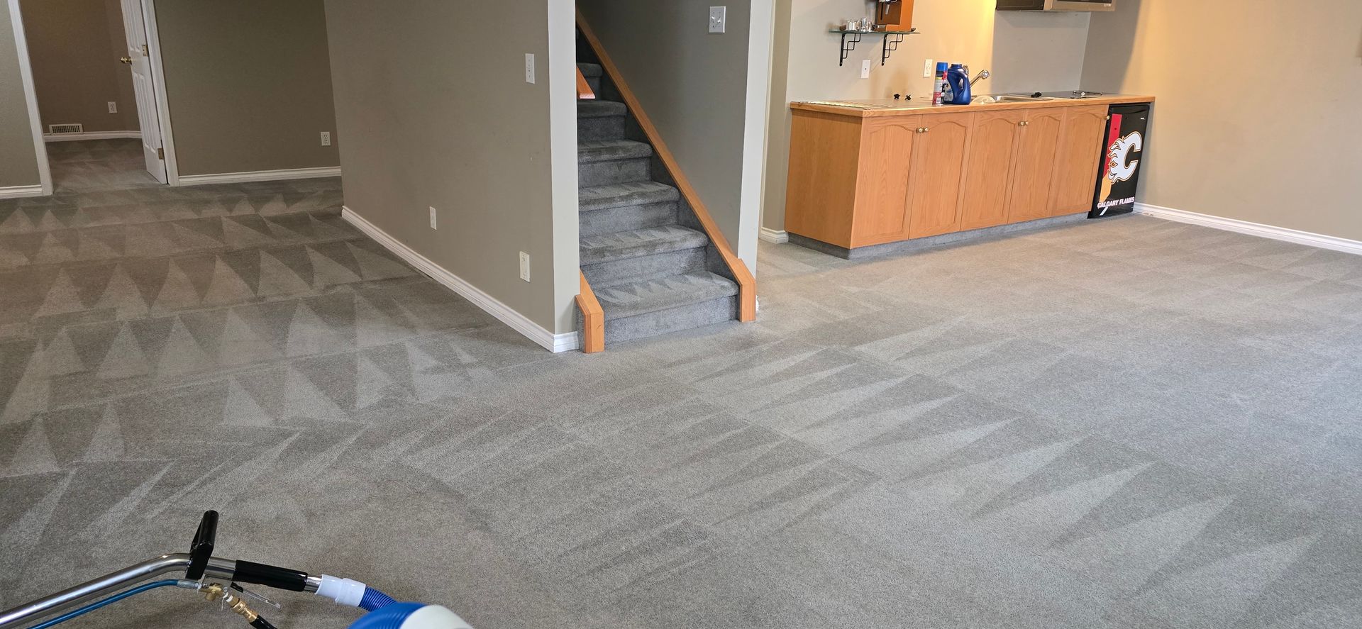 Carpeted room with stairs, cabinets, and cleaning equipment.