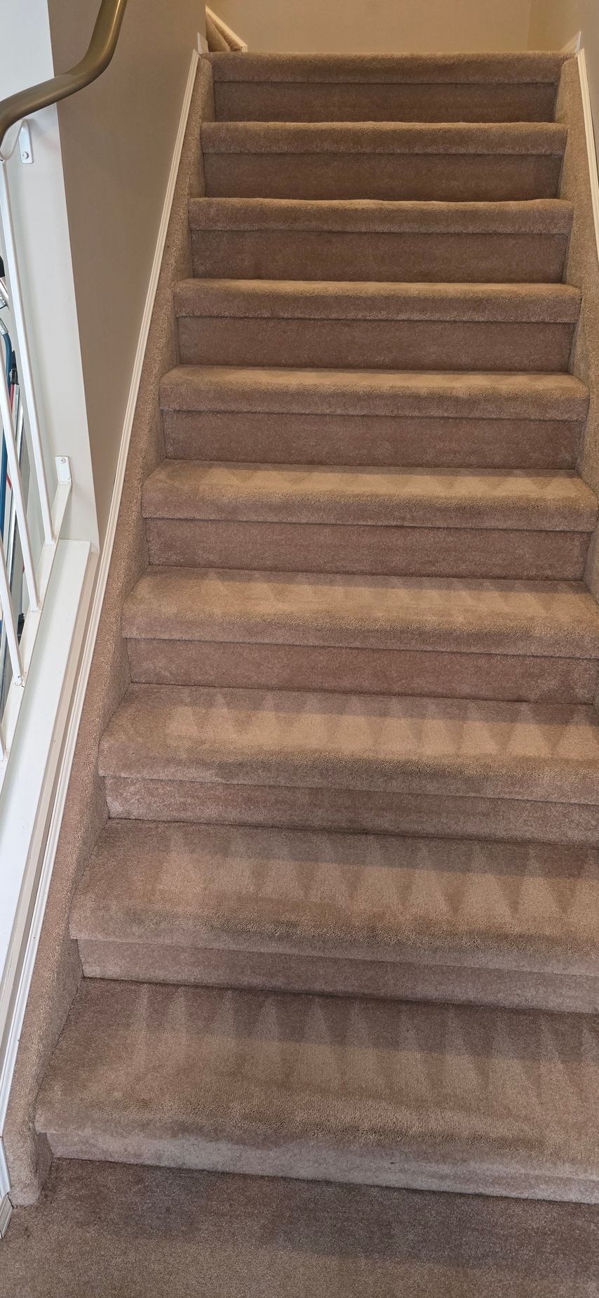 Carpeted staircase, beige, with a white banister and handrail, leading upwards.