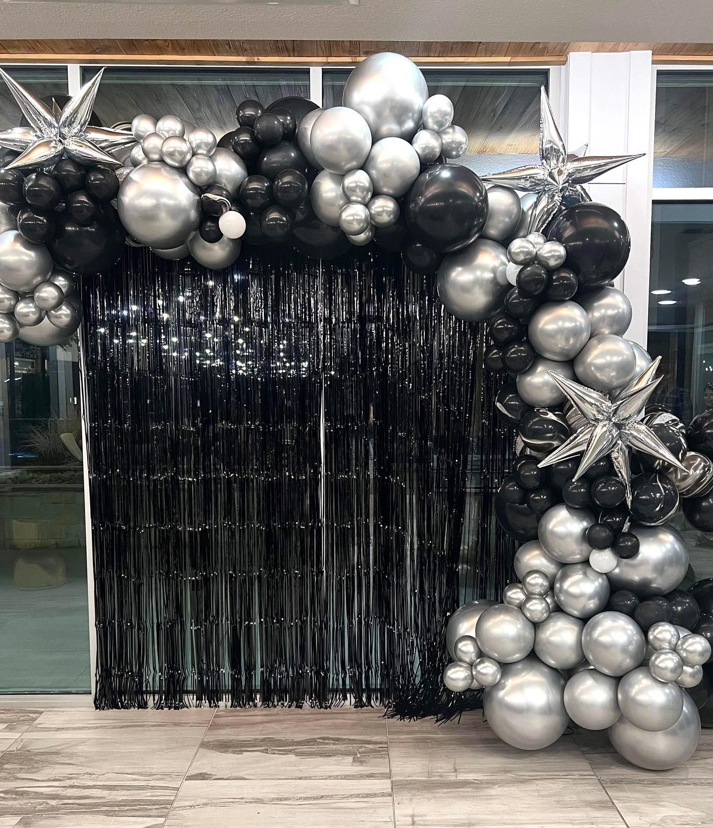 A bunch of black and silver balloons are sitting in front of a black curtain.
