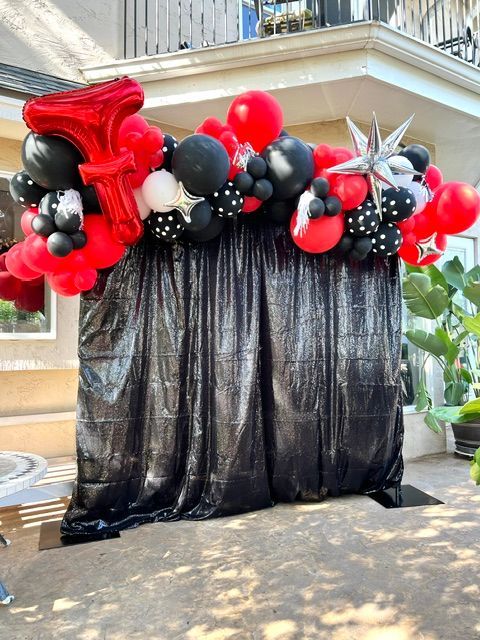 A black curtain is covered in red , black and white balloons.