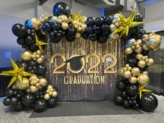A wall decorated with black and gold balloons and stars for a graduation party.