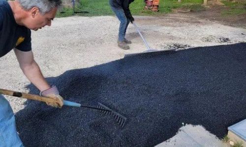 Technician applying asphalt seal coating and performing maintenance on a driveway surface