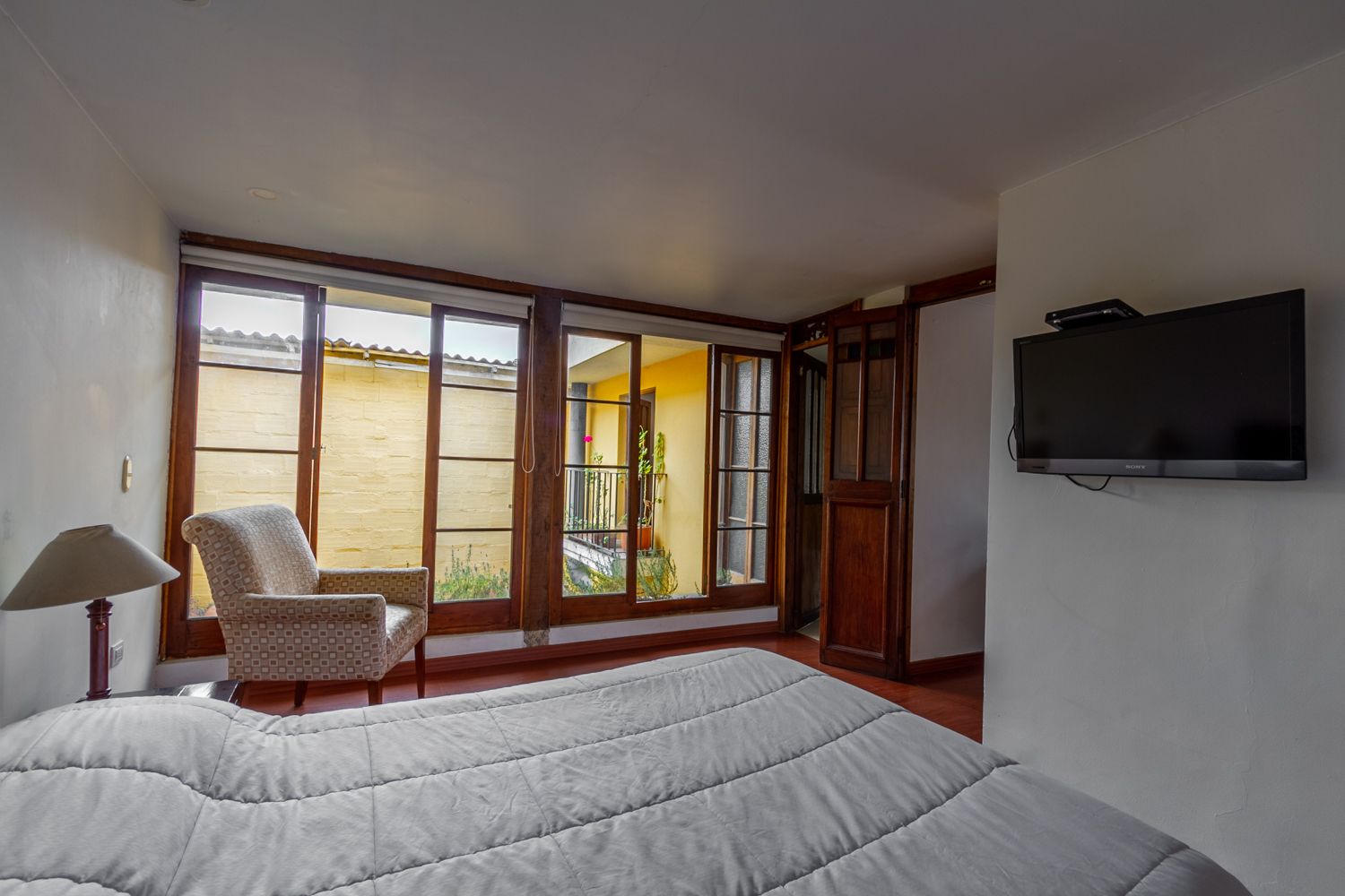 A bedroom with a bed , chair , television and lots of windows.