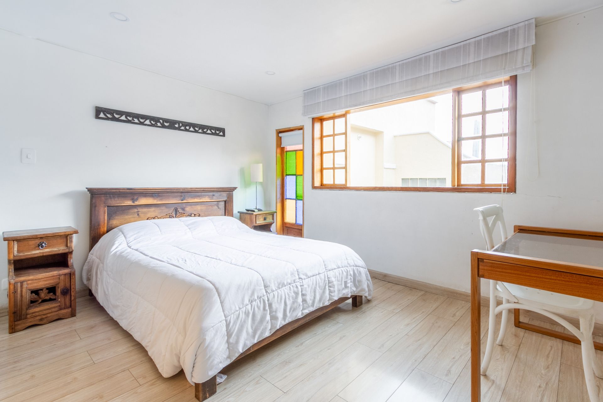 A bedroom with a bed , nightstand , desk and window.