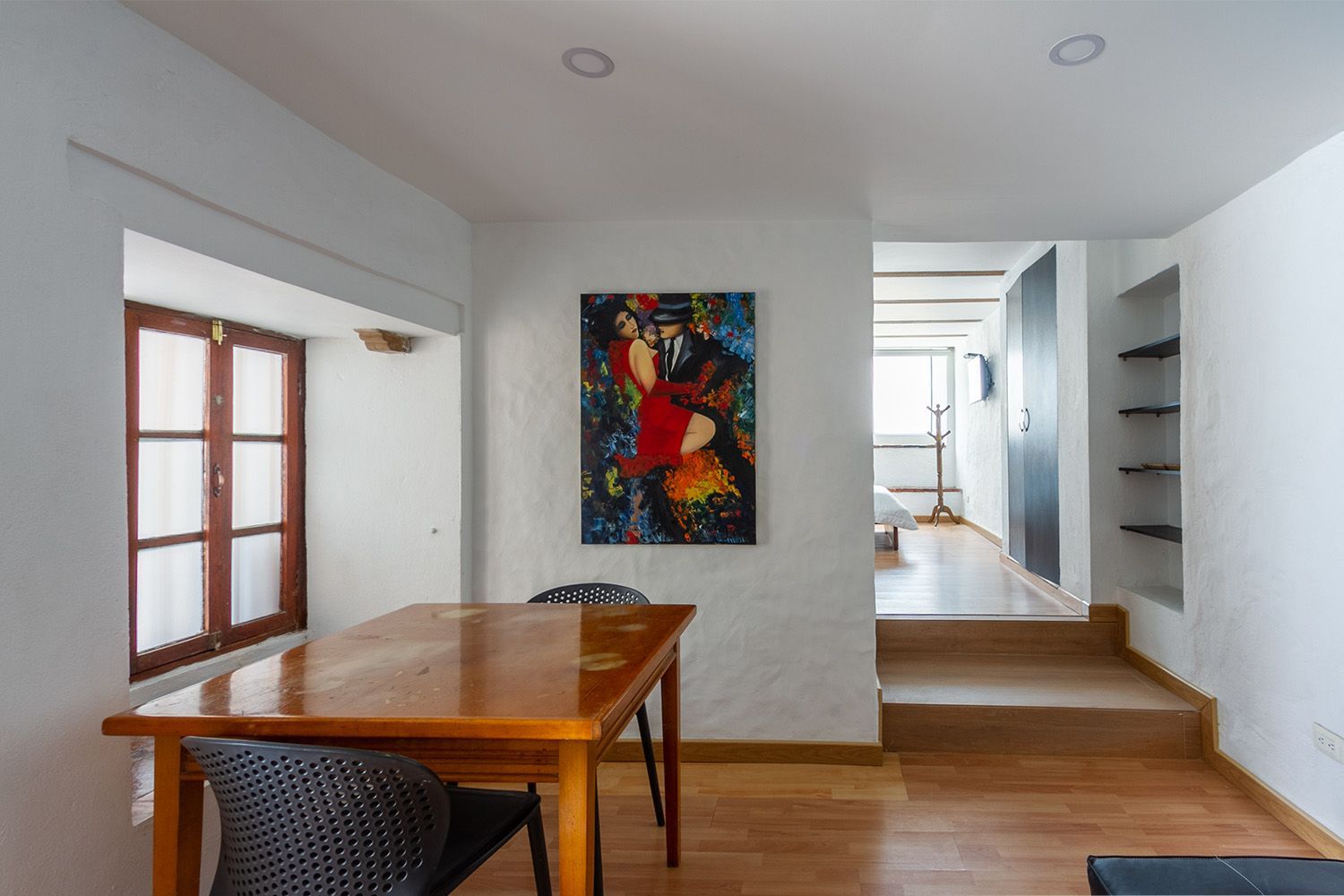 A dining room with a table and chairs and a painting on the wall.
