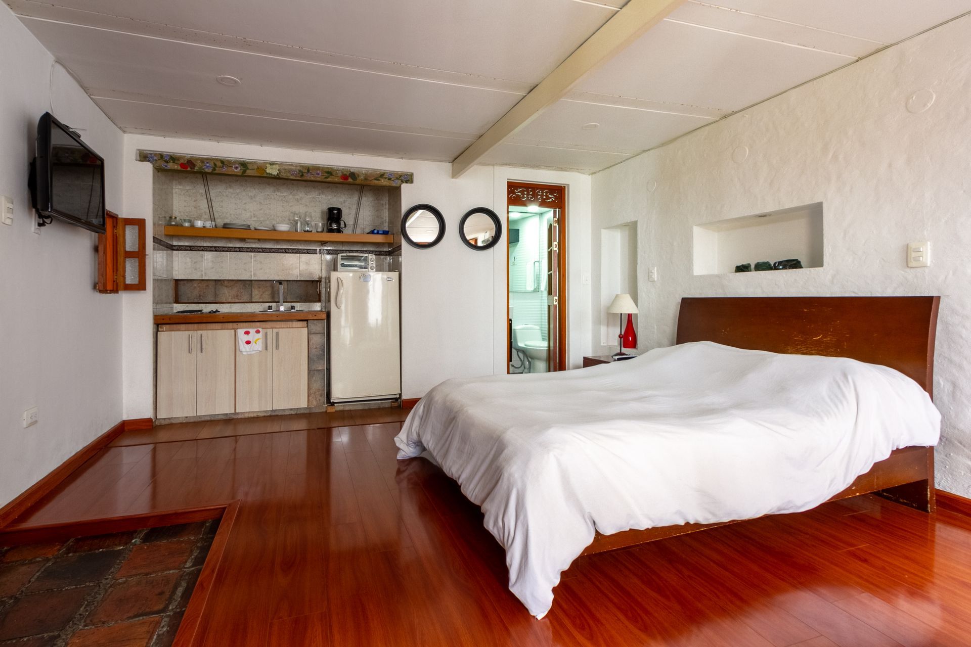 A bedroom with a large bed and a kitchen in the background